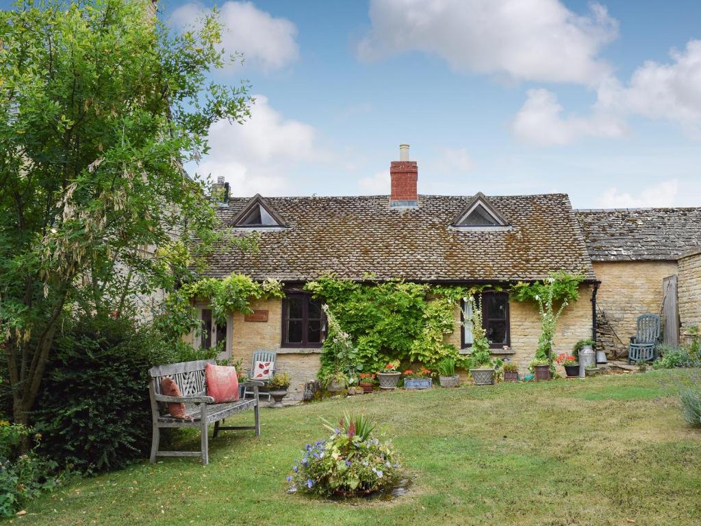 una casa vieja con un banco en el patio en Picket Piece Cottage, en Chadlington