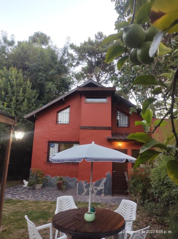 una mesa con sombrilla frente a una casa roja en La Casa Del Bosque en Mar del Plata