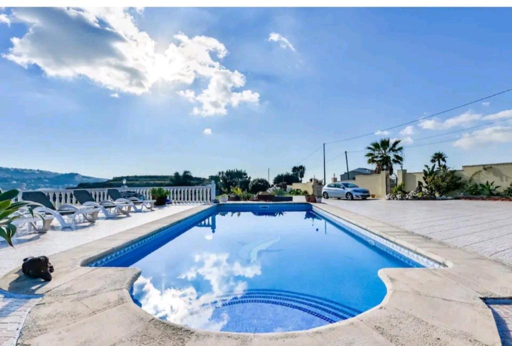 a swimming pool with chairs and a blue sky at Casa de vacaciones con piscina comunitaria in Teulada