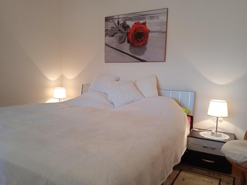 ein Schlafzimmer mit einem weißen Bett mit einer roten Rose an der Wand in der Unterkunft Fonyódi Centrum Apartman in Fonyód