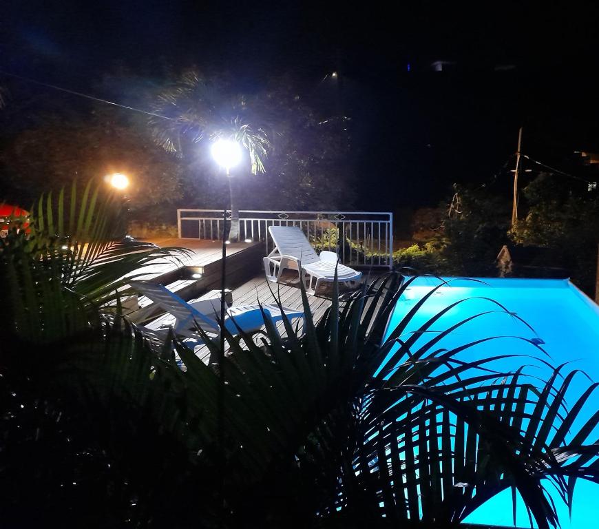 a pool at night with two chairs and a light at BEL APPARTEMENT T2 LUMINEUX in Les Anses-dʼArlets