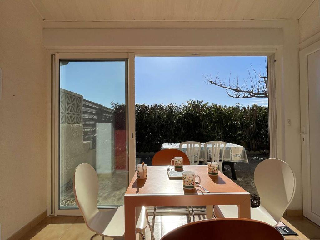 une salle à manger avec une table et des chaises et une grande fenêtre dans l'établissement Pavillon calme à Narbonne Plage, 6 couchages, grande terrasse, piscine et parking privé - FR-1-229B-67, à Narbonne