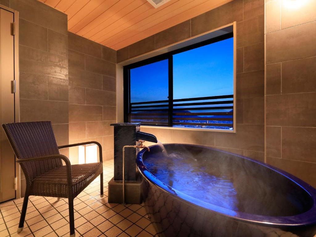 a large tub in a bathroom with a chair and a window at Hotel Tsubakino in Yamanouchi