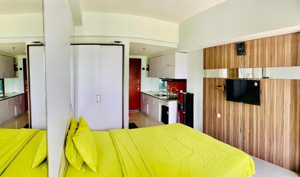 a bedroom with a yellow bed and a kitchen at Apartemen Mahogany By Ruang Sultan in Karawang