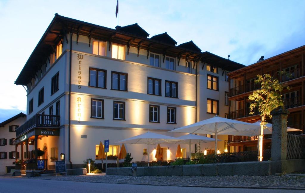 un grand bâtiment blanc avec des parasols en face de celui-ci dans l'établissement Hotel Weisses Kreuz Bergün, à Bergün