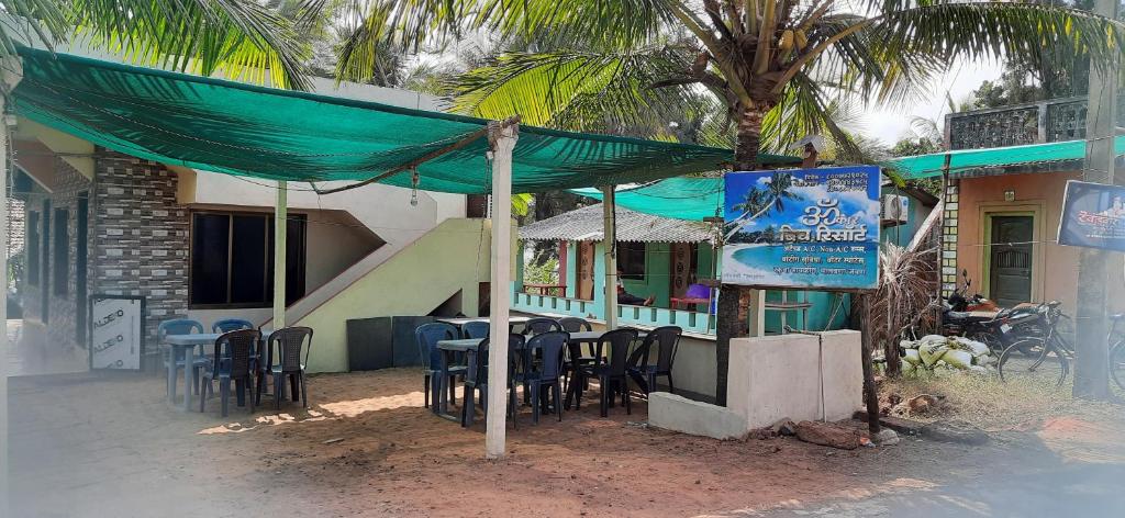 Omkar Beach Resort في مالفان: مطعم بطاولات وكراسي تحت مظلة خضراء