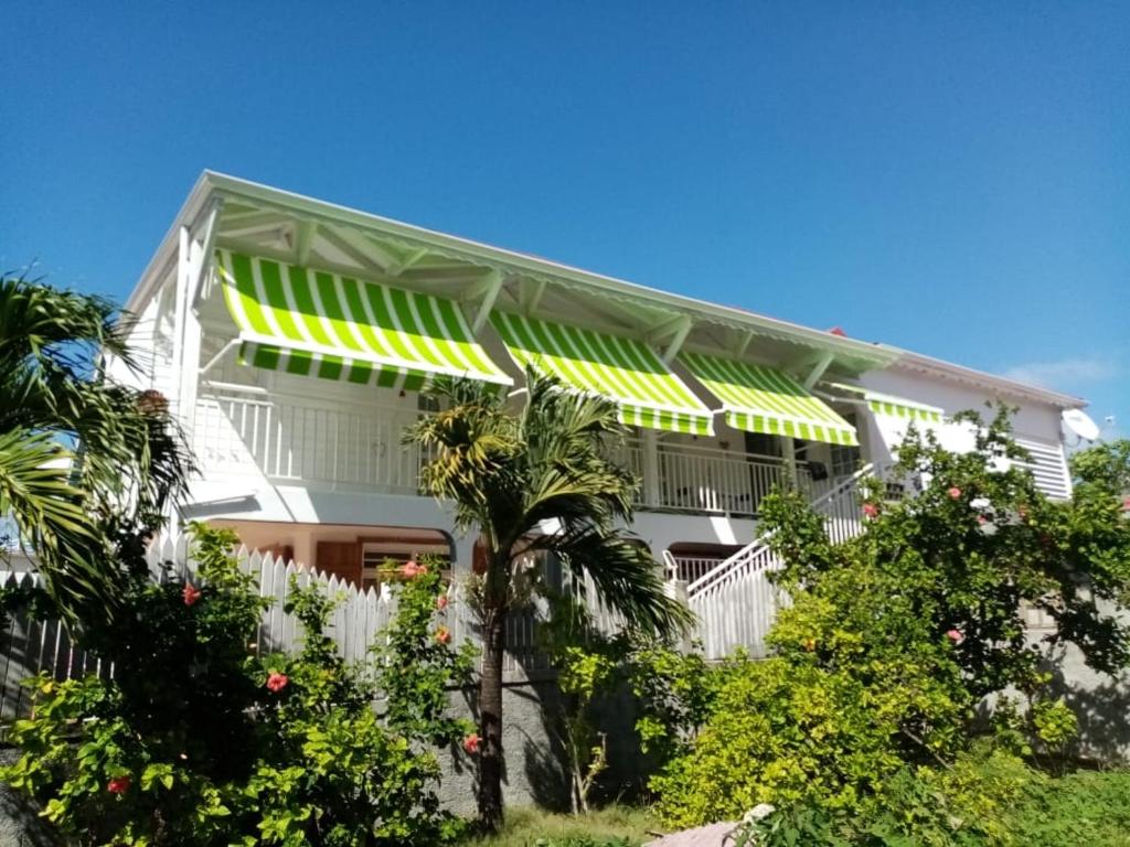 una casa blanca con toldos verdes y árboles en Chez Tata et Didi, en Grand-Bourg