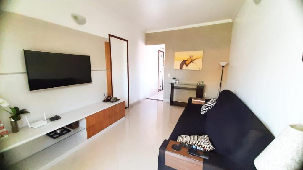 sala de estar con sofá y TV en la pared en Sobrado a 1 quadra da Praia dos Anjos, en Arraial do Cabo