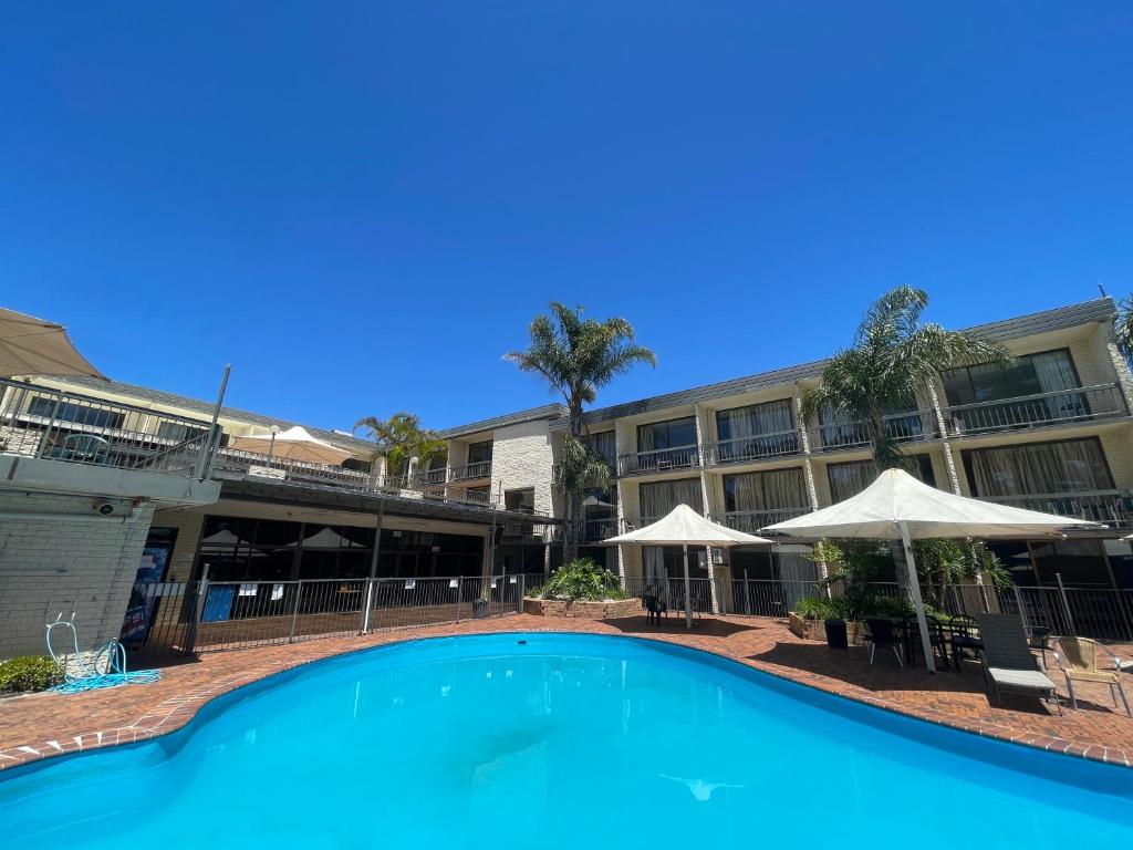 a swimming pool in front of a building with umbrellas at El Lago Waters Resort in The Entrance