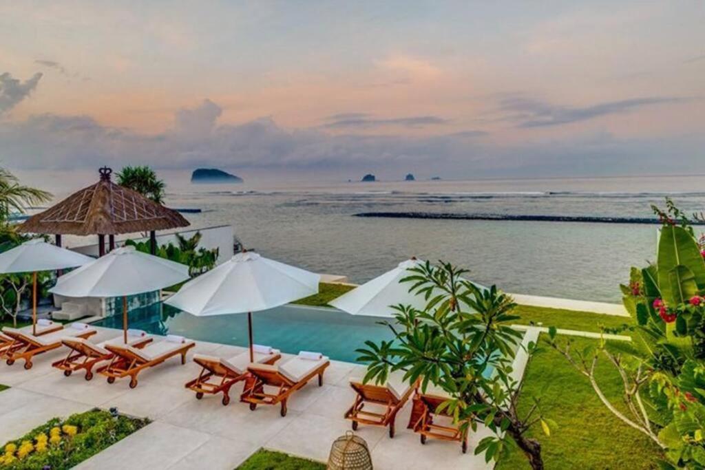 a pool with chairs and umbrellas and the ocean at Villa Oceana, Candidasa in Candidasa