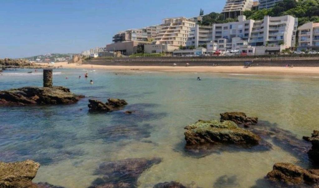 a beach with people in the water and buildings at 84 Camarque Umdloti beach in Umdloti