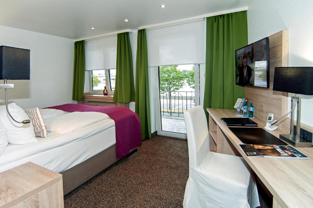 ケルンにあるホテル アレグロのベッド、デスク、窓が備わるホテルルームです。