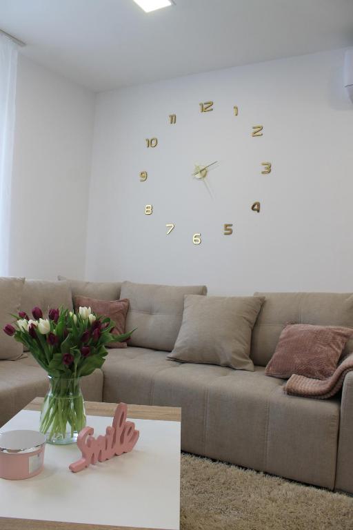 a living room with a couch and a clock on the wall at Flower Apartman 4 