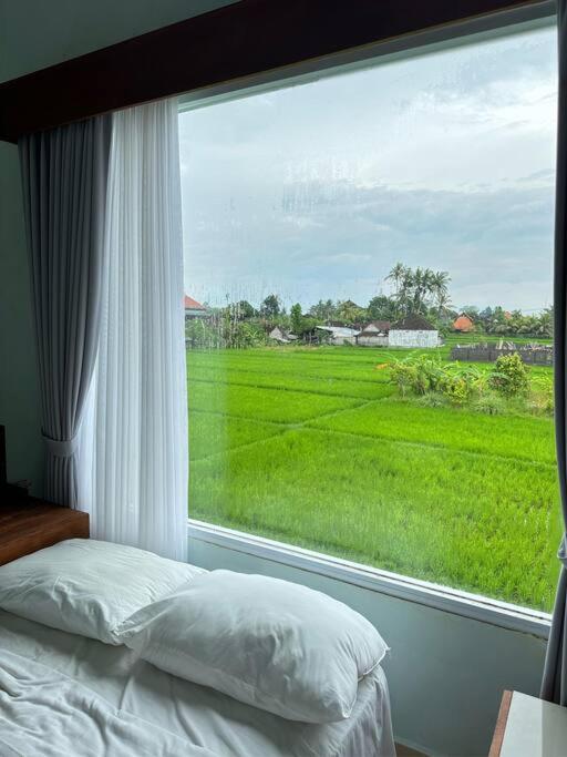 een slaapkamer met een groot raam met uitzicht op een groen veld bij Manis House with ricefield view very close to ubud in Ubud