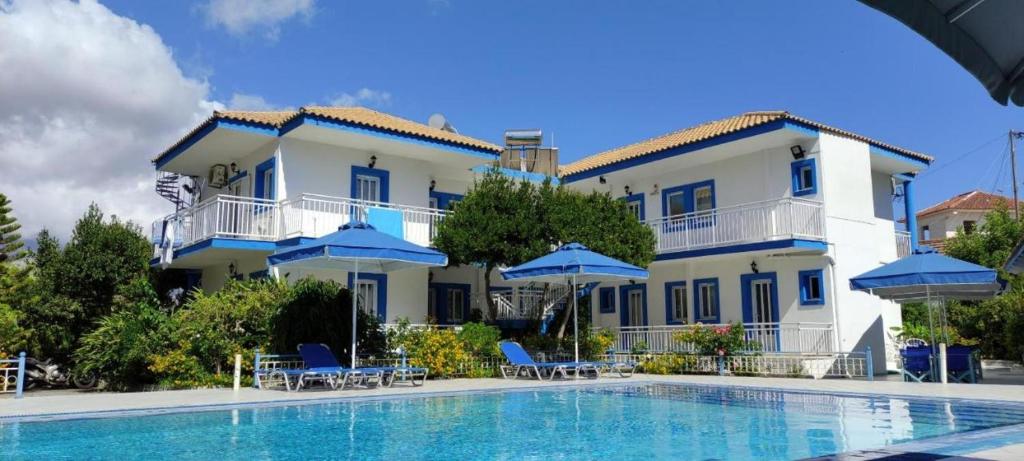 duży budynek z basenem i niebieskimi parasolami w obiekcie Blue White Apartments w mieście Kefalonia