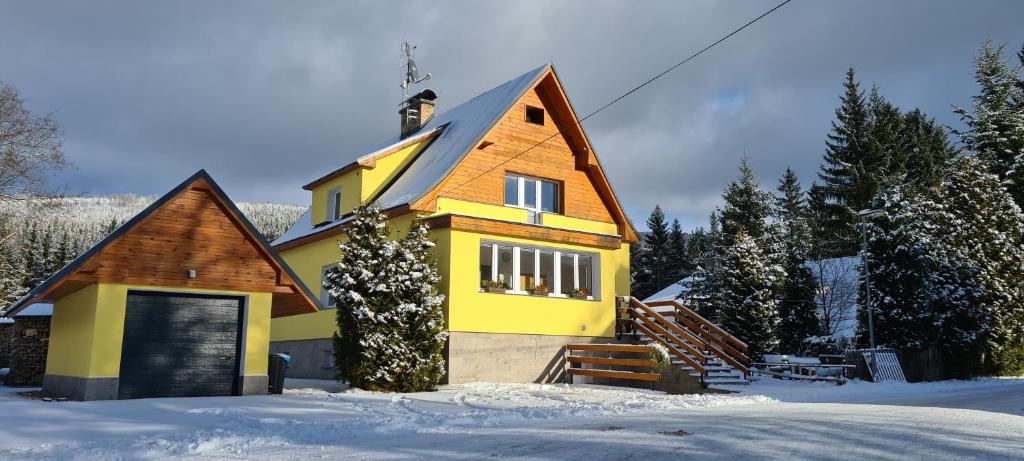 una casa amarilla con techo de gambrel en la nieve en Apartmány Mamut Harrachov, en Harrachov