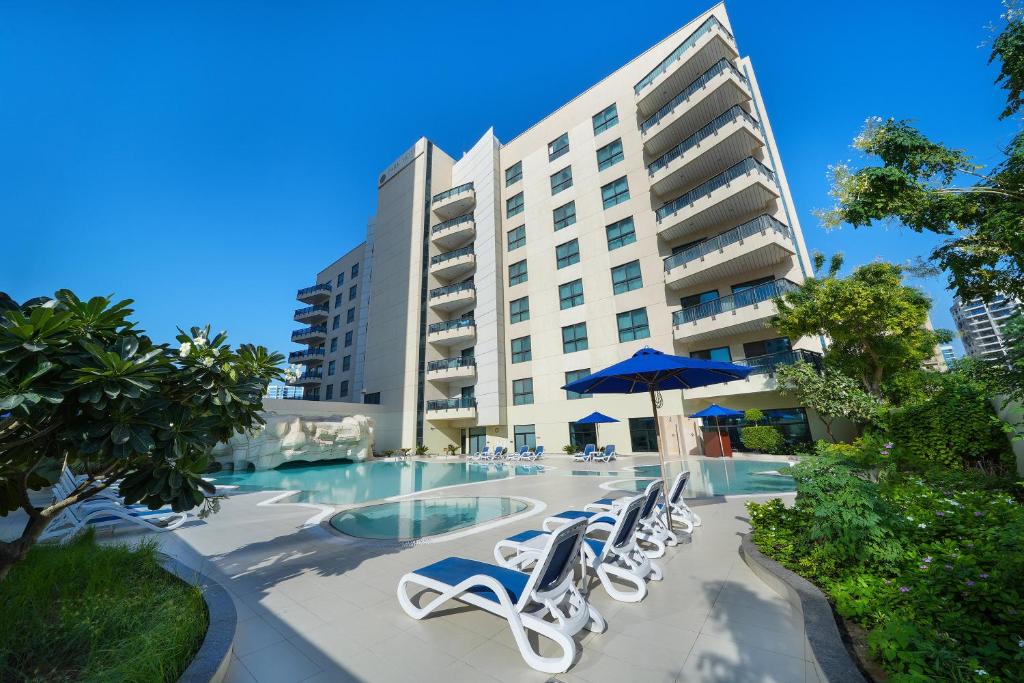 a pool with chairs and an umbrella and a building at Park Apartments Dubai, an Edge By Rotana Hotel in Dubai