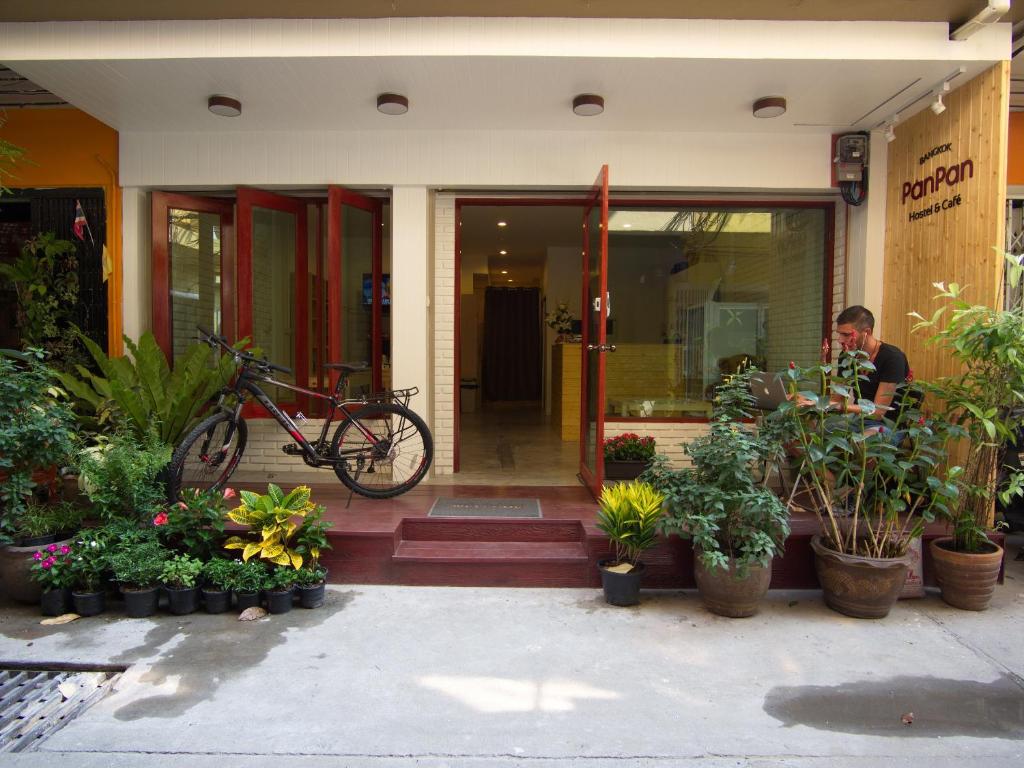 a man sitting in front of a building with plants at PanPan Hostel in Bangkok