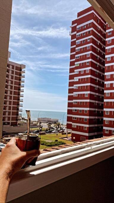 a person holding a cup of coffee looking out a window at Departamento 3 ambientes vista al mar en Playa Grande con cochera cubierta in Mar del Plata