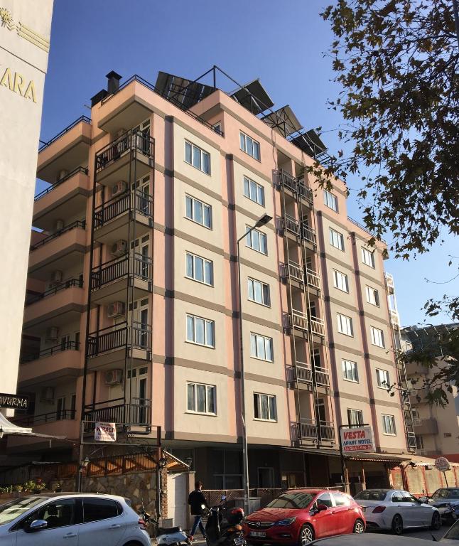 a tall building with cars parked in front of it at Vesta Apart Hotel in Kuşadası