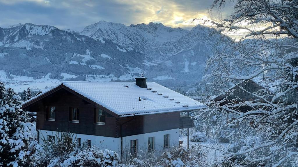 a house covered in snow with mountains in the background at Ferienwohnung Panoramablick in Bolsterlang