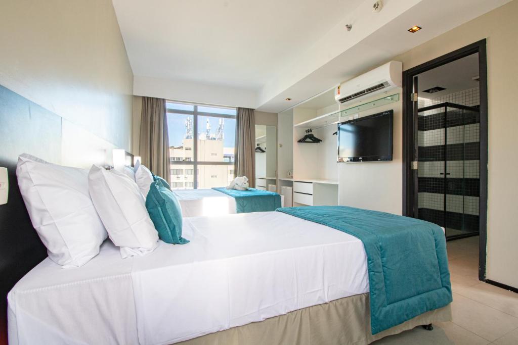 a bedroom with a large white bed and a television at Acqua Prime Maceió Ponta Verde in Maceió