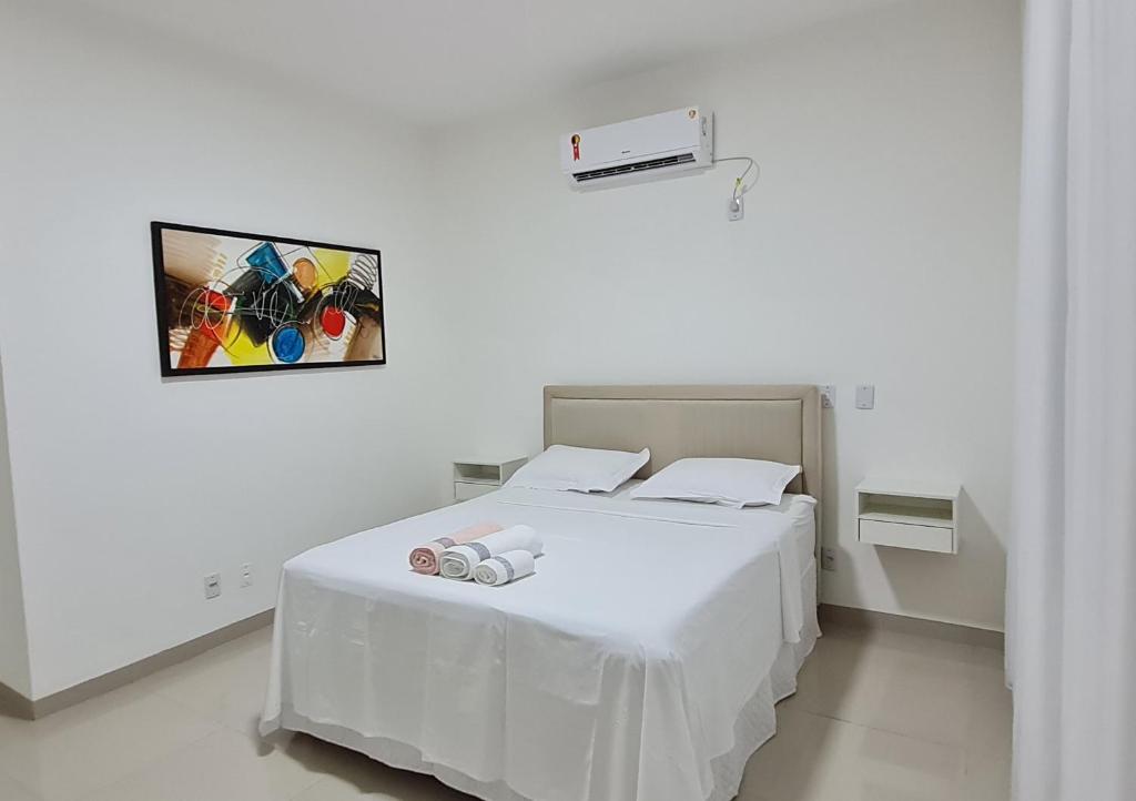 uma cama branca num quarto branco com uma fotografia na parede em Apartamento no centro próximo a JK. em Palmas