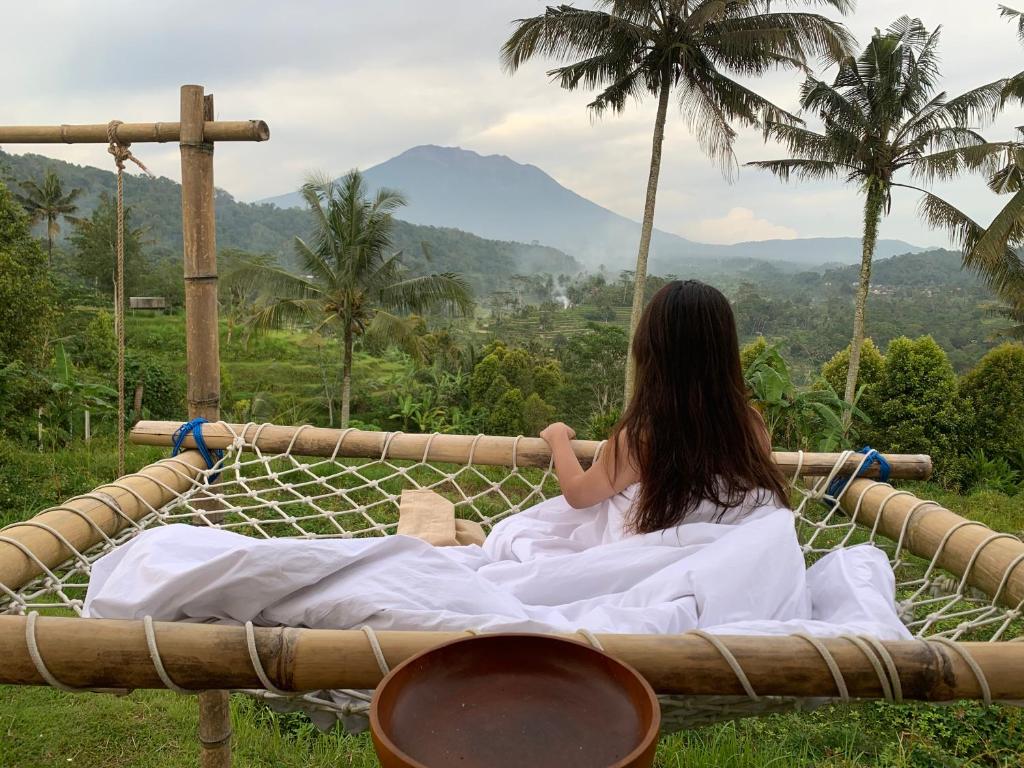 une femme assise dans un hamac donnant sur les montagnes dans l'établissement Gladak di Uma Bali, à Sidemen