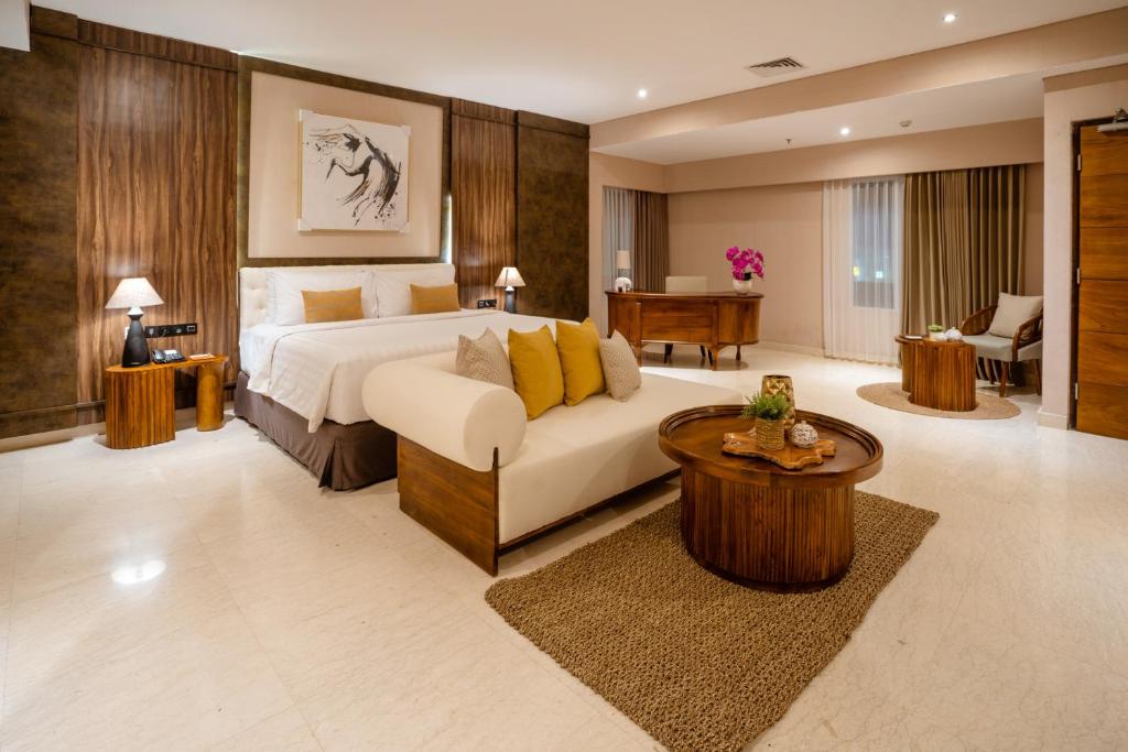 a bedroom with a bed and a couch and a table at Crystalkuta Hotel - Bali in Kuta