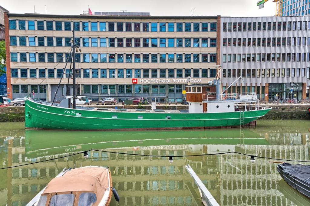 een groene boot in het water voor een gebouw bij Boathotel Rotterdam Wilhelmina in Rotterdam