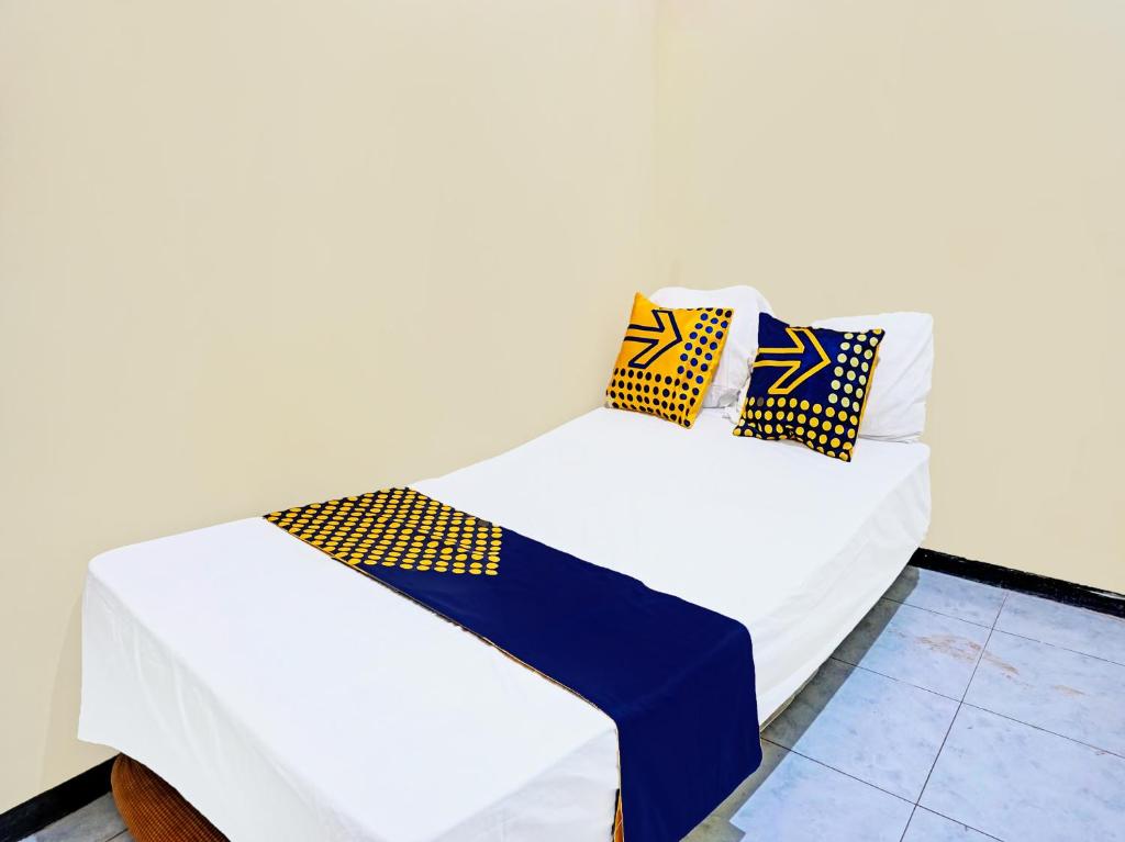 a white bed with blue and yellow pillows on it at OYO Life 92091 Citra Omah Syariah in Blimbing