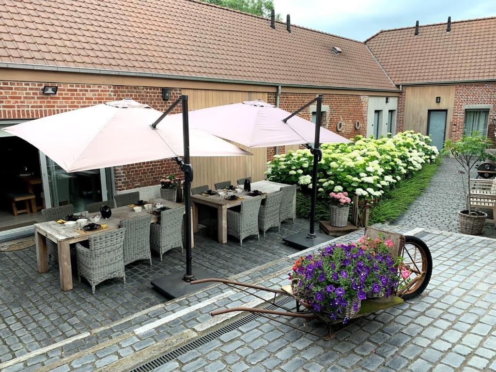 un patio al aire libre con mesas, sombrillas y flores en B&B 't Oezent en Oudenaarde