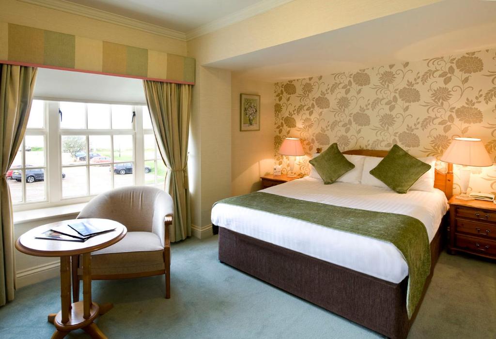 a hotel room with a bed and a chair and a window at Old Hunstanton Le Strange Arms Hotel in Hunstanton