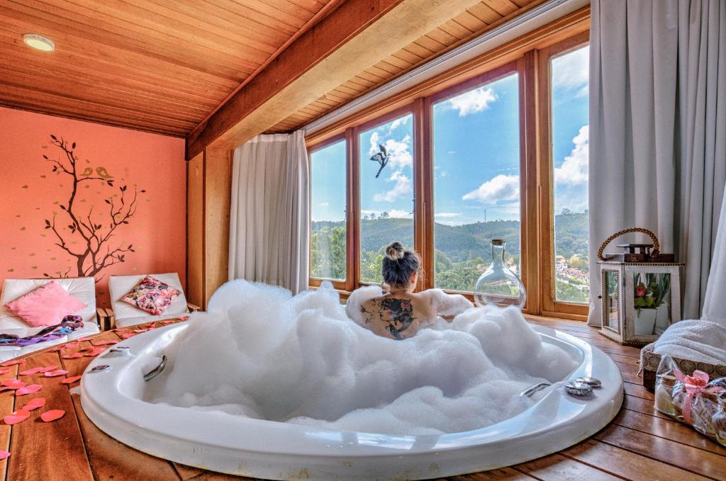 a woman laying in a large bath tub in a room with windows at Carícia do Vento Pousada Boutique in Monte Verde