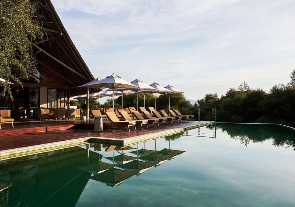 a swimming pool with lounge chairs and umbrellas at Letamo at Qwabi Private Game Reserve by NEWMARK in Bela-Bela