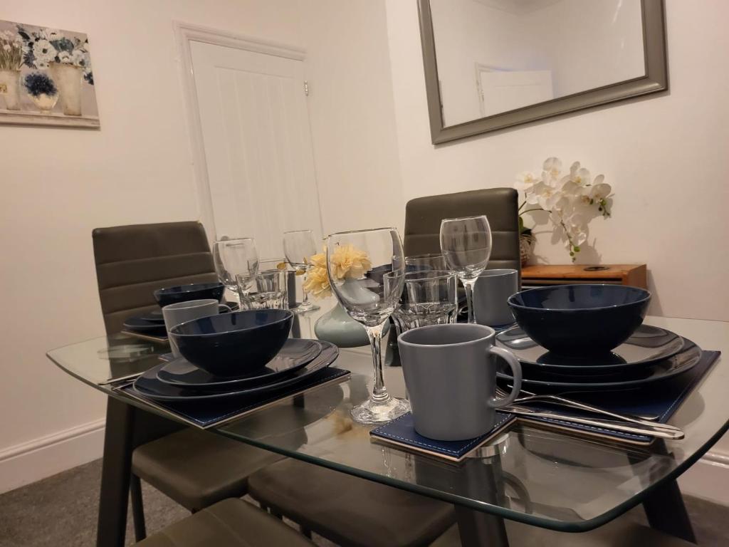 a glass table with plates and wine glasses on it at Homey Bella House in Luton