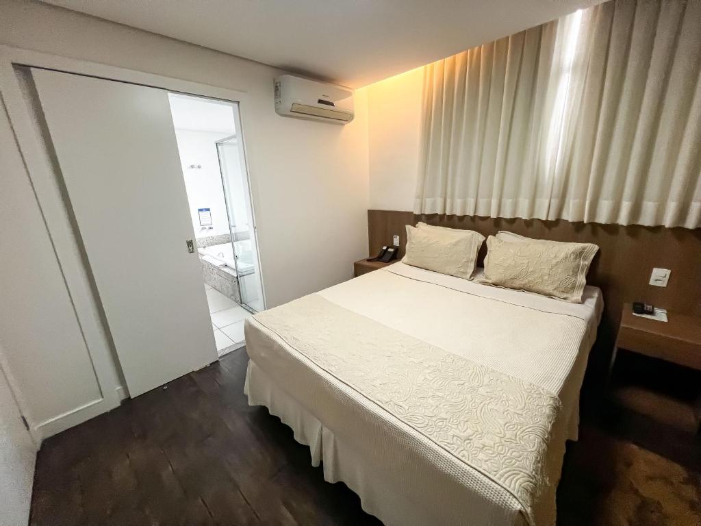 um quarto com uma cama branca e uma porta de vidro deslizante em Nobile Hotel Belo Horizonte em Belo Horizonte