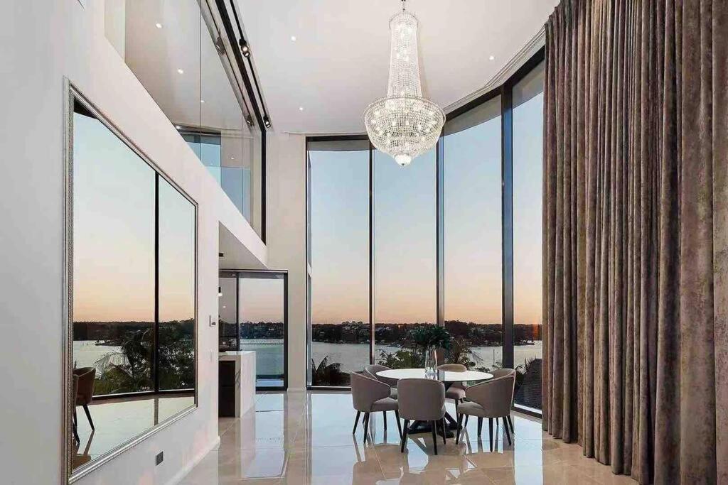 a dining room with a table and chairs and large windows at SYD Luxury cheerful water view holiday house in Sydney