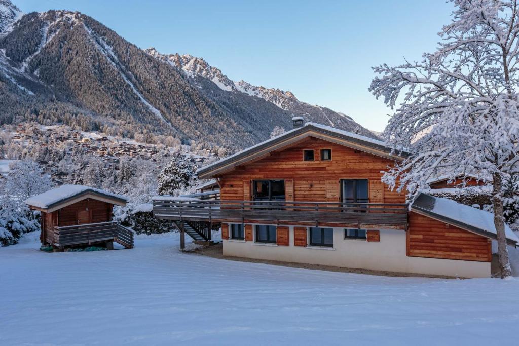 una cabaña de madera en la nieve con montañas en el fondo en Chalet De L'ours - Chamonix All Year, en Chamonix-Mont-Blanc