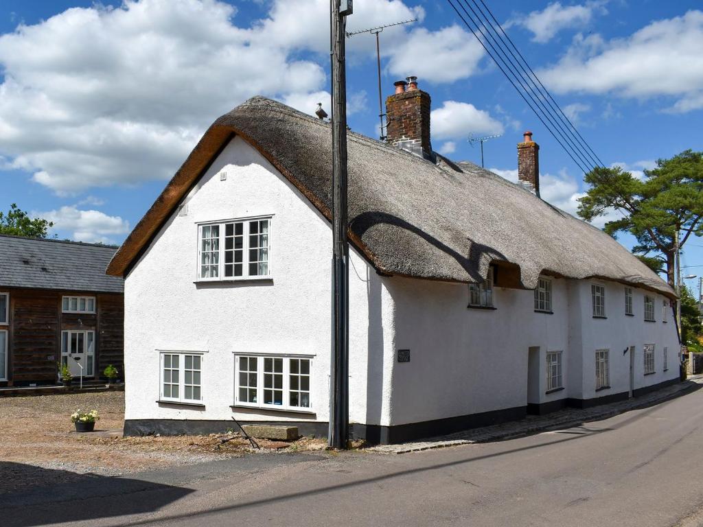 a white building with a thatched roof at Glimsters Cottage in Kentisbeare