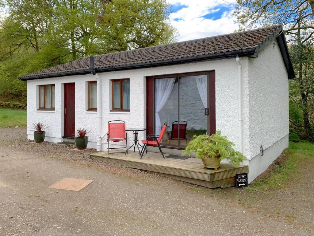 a small white cottage with red chairs on a porch at Crossburn Hideaway in Helensburgh
