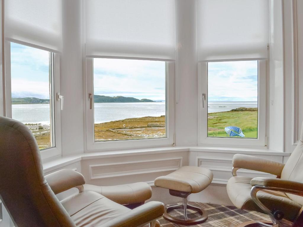 a room with three windows with chairs and a table at Thornbank in Millport