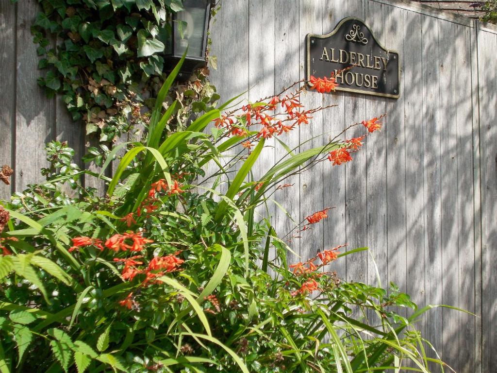 een bord op een hek met planten en bloemen bij Alderley House in Bourton on the Water