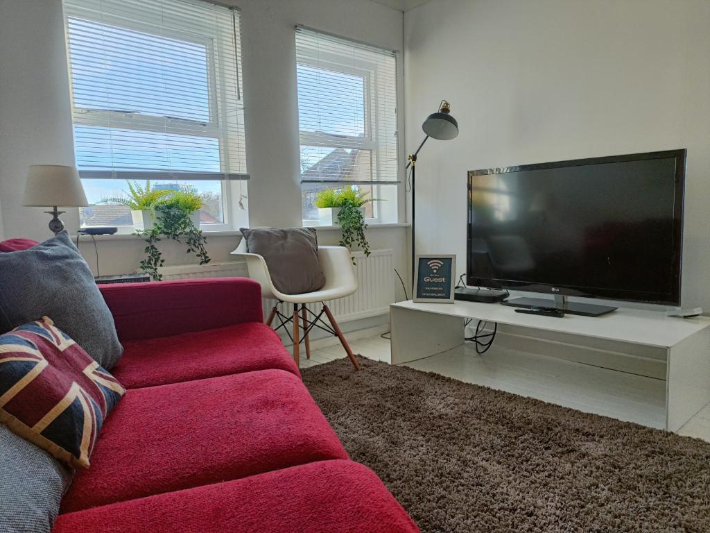 a living room with a red couch and a flat screen tv at 2 Bed Functional House Close to Manor Park Train Station in London