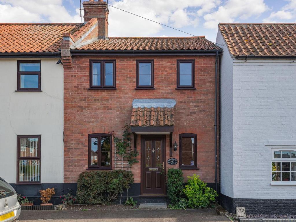 uma casa de tijolos vermelhos com uma porta castanha em Nightingale Cottage em Castle Acre