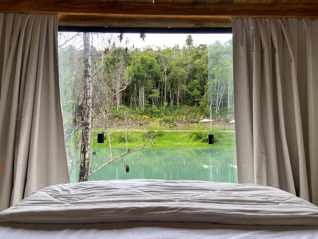 a bedroom with a large window with a view of a lake at Chalés da Floresta in Porto Seguro