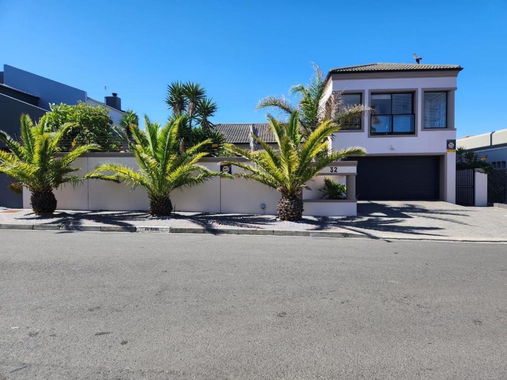 a house with palm trees in front of a driveway at Balmoral Cottage, West Beach in Cape Town