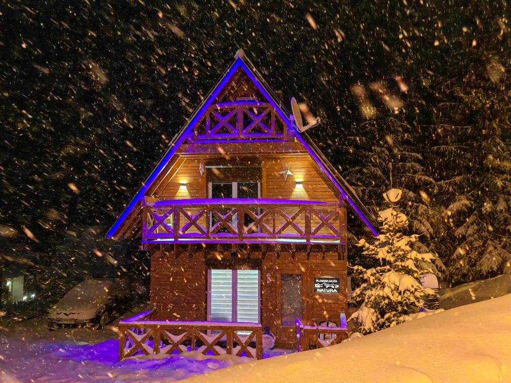 ein Haus mit lila Lichtern im Schnee in der Unterkunft Planinska kuca NATURA in Vlasic