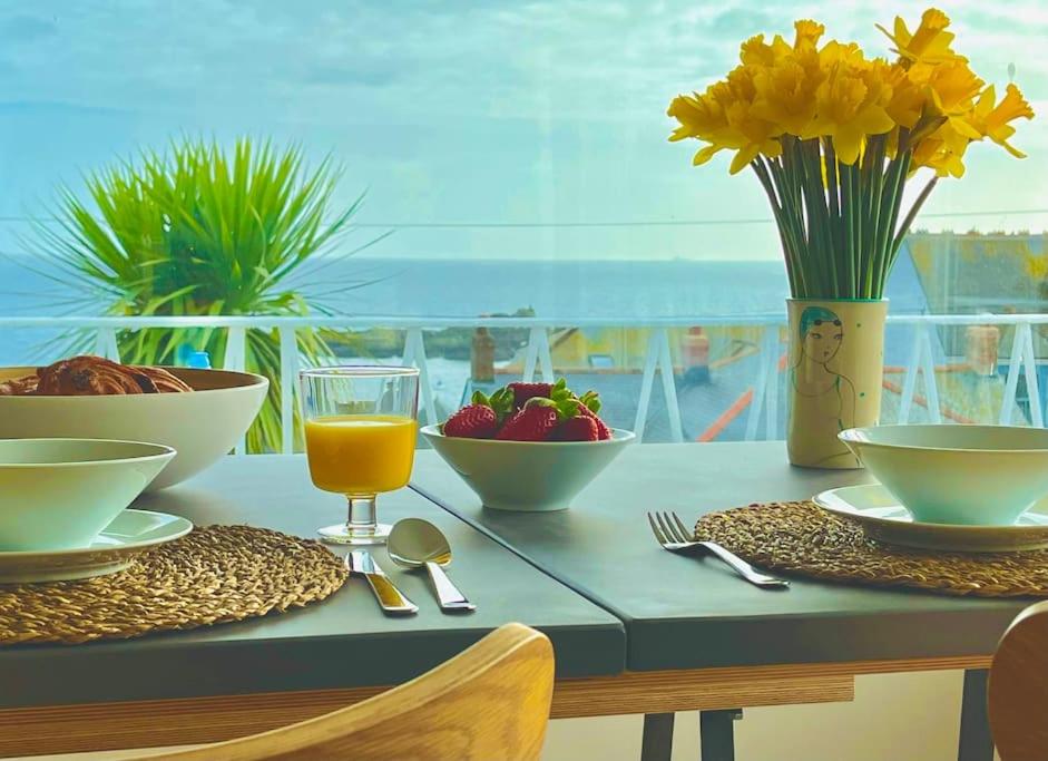 a table with food and flowers and a glass of orange juice at Spacious home with panoramic sea view, free parking EV & large garden in Mousehole