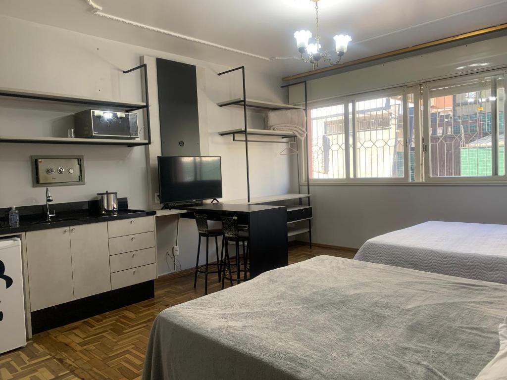 a bedroom with two beds and a desk and a kitchen at Pousada Hostel Dodora in Bento Gonçalves